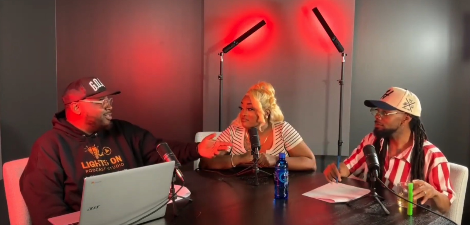 Lights On Podcast Studio session in progress — host in branded hoodie with two guests under signature red lighting